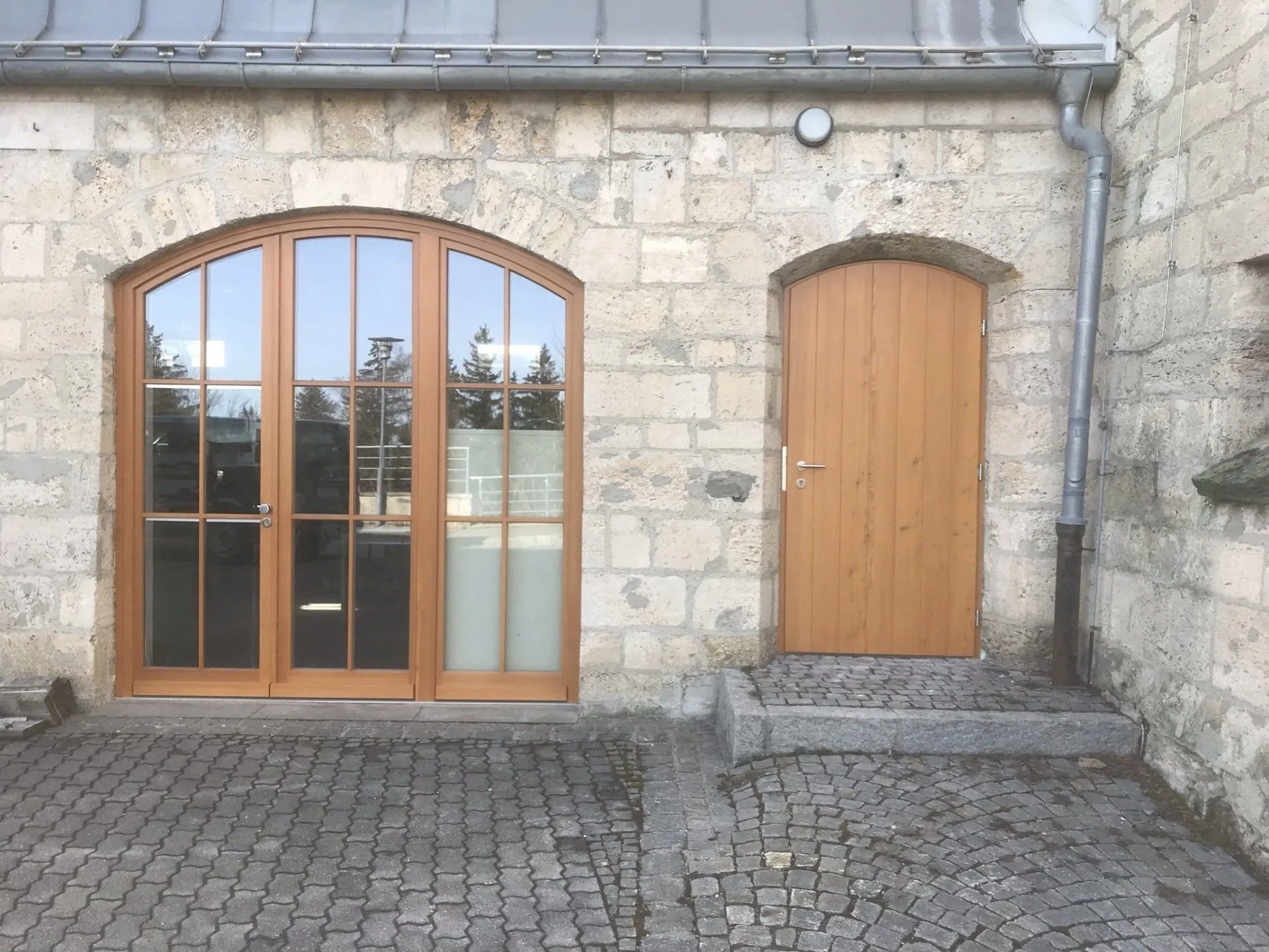 Rundbogenfenster und Haustür aus Holz in einer Natursteinfassade